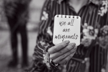 Person holding card on which is written we are all migrants ©Shutterstock 